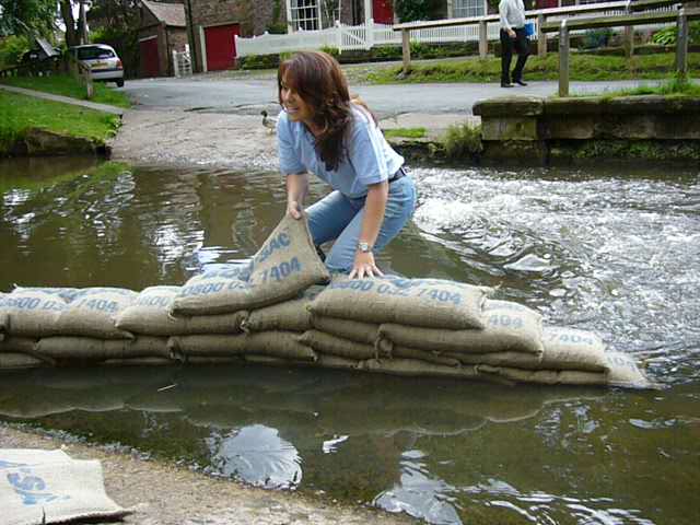 Lady up to her angles in flood building a sandbag wall